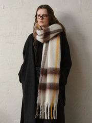 Woman wearing a long dark coat and a large plaid scarf with white, brown, and yellow stripes, with the scarf draped around her neck.