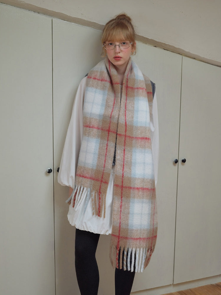 Woman wearing a large plaid scarf draped over a white shirt and grey vest.