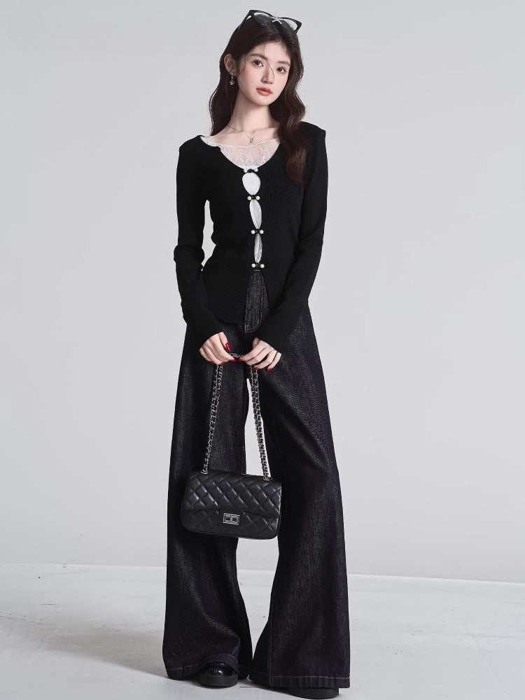 Full body shot of a woman wearing a black long-sleeved top with white lace trim and decorative buttons, dark wide-leg jeans, and carrying a black quilted handbag.