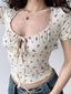 Close-up of a cream-colored, short-sleeved crop top with a blue floral print and a tie-front detail.