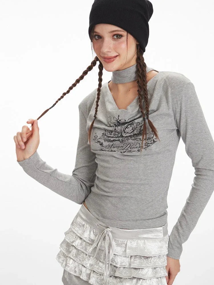 Close-up of a model's upper body and face wearing a grey long-sleeved top with a graphic print and choker detail, black beanie, playing with her braided hair.