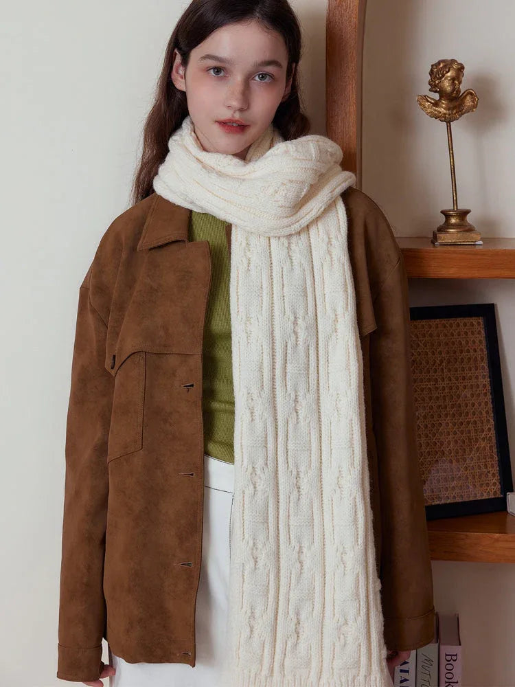 Front view of a woman wearing a cream-colored cable knit scarf and brown jacket.