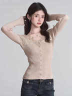 Woman posing with hands behind her head, wearing a beige ribbed knit cardigan with lace trim and a v-neck, paired with dark wash jeans.