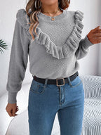 woman wearing a grey knit sweater with ruffle trim, blue jeans, and a black belt from the front