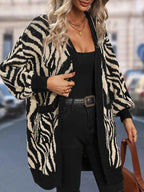 Woman wearing a black and white zebra print longline knit cardigan, adjusting the cardigan with her hand.