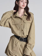 Model wearing a tan button-down shirt dress with a black studded belt and dark brown boots.