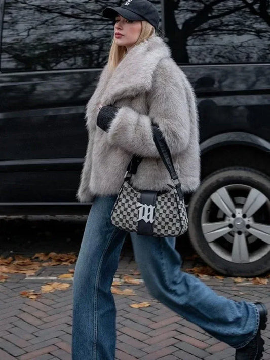 Woman walking in a light grey oversized faux fur jacket with a black baseball cap and blue jeans