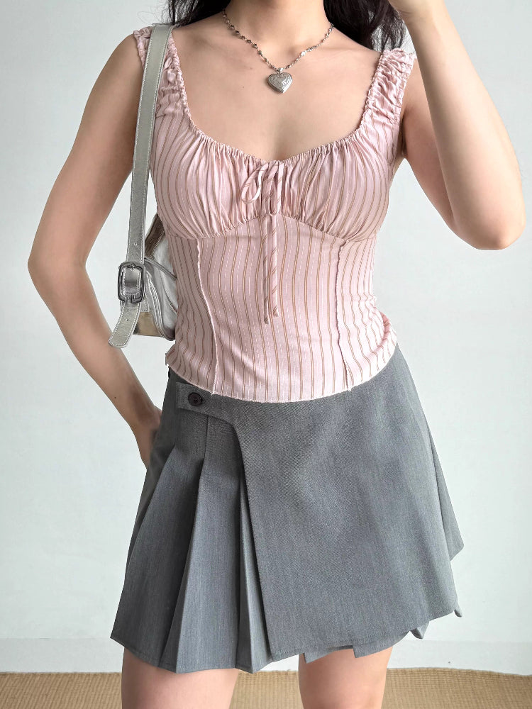 Woman wearing a pink striped ribbed knit top and a grey pleated skirt with a button accent.