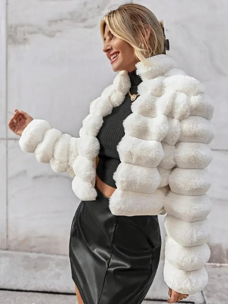 Woman wearing a white faux fur cropped jacket over a black top and black skirt, smiling outdoors. Main image