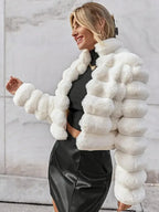 Woman wearing a white faux fur cropped jacket over a black top and black skirt, smiling outdoors.