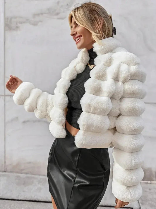 Woman wearing a white faux fur cropped jacket over a black top and black skirt, smiling outdoors.