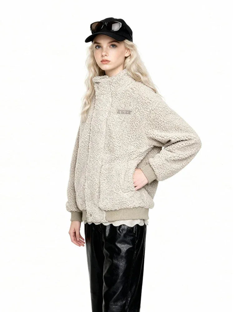 Woman in a cream-colored sherpa fleece bomber jacket, black faux leather pants, and a black baseball cap with sunglasses, with hand in pocket.