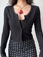 Close-up of a black cropped knit cardigan with lace trim and a black polka dot skirt.