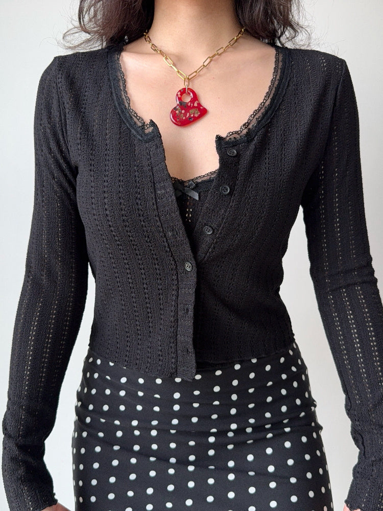 Close-up of a black cropped knit cardigan with lace trim and a black polka dot skirt.