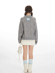 Back view of a model wearing a grey knitted cardigan with a white textured mini skirt.
