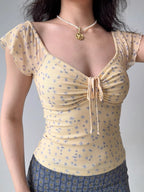 Close-up of a yellow floral print mesh top with a ruched tie front and short flutter sleeves.