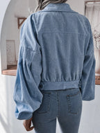 Back view of a woman wearing a light blue corduroy cropped jacket with balloon sleeves and blue jeans.