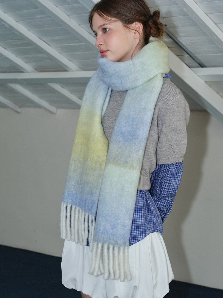 Side profile of a woman wearing an oversized ombre scarf draped over her shoulders.