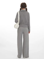 Back view of a woman wearing a grey knit zip-up jacket and wide-leg pants with a white shoulder bag.