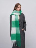 Woman wearing a grey coat and a green and white plaid scarf with fringe.