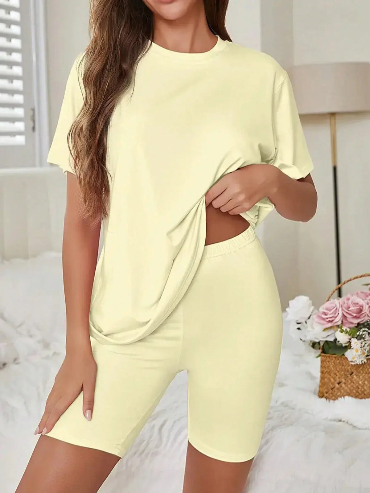 Woman in a light yellow t-shirt and biker shorts set lifting the hem of her shirt.
