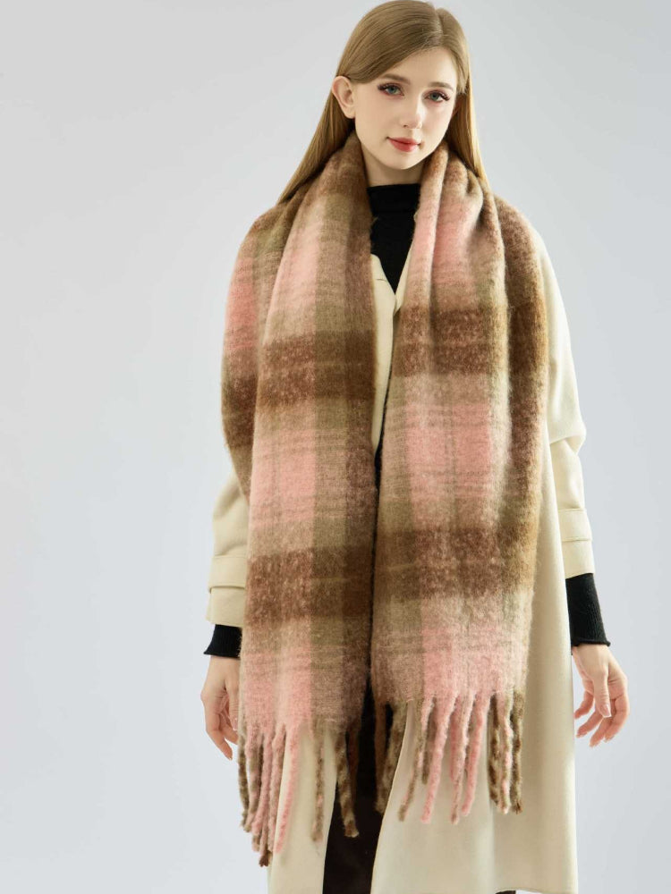 Woman in a cream coat with a large, soft plaid scarf in pink and brown draped around her neck.