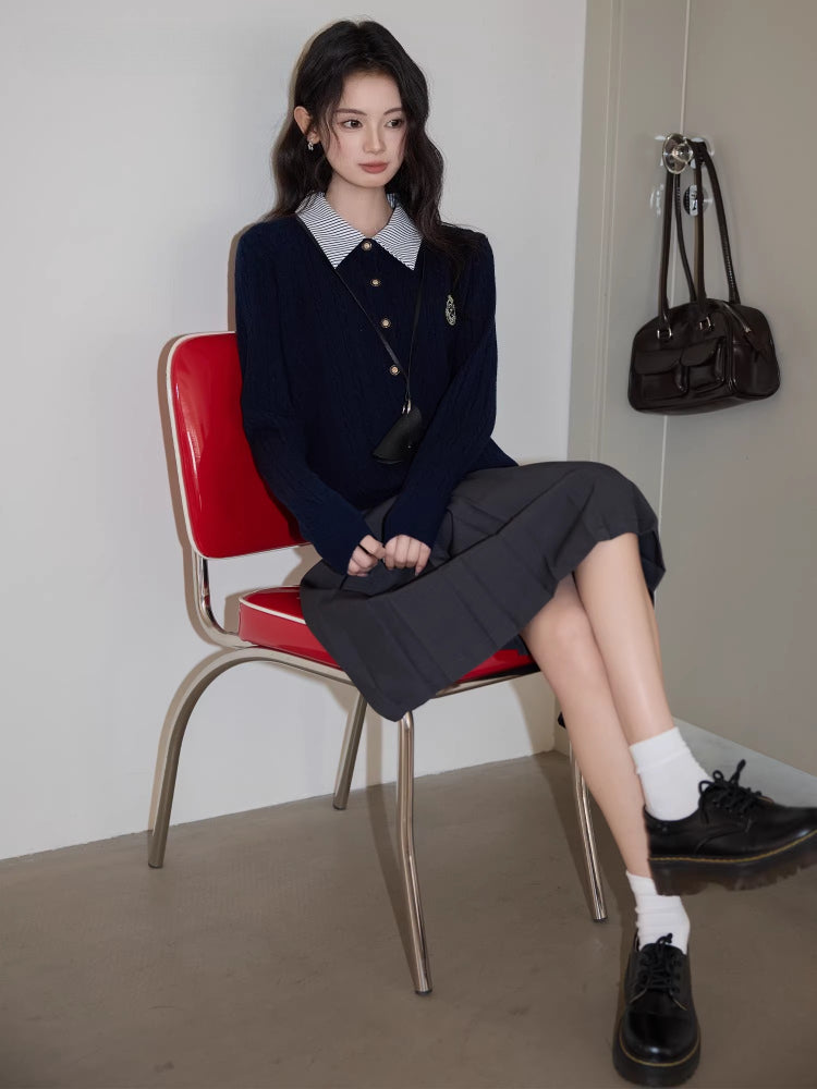 Woman sitting on a red chair wearing a navy blue cable knit cardigan with a striped collar and a gray pleated skirt.