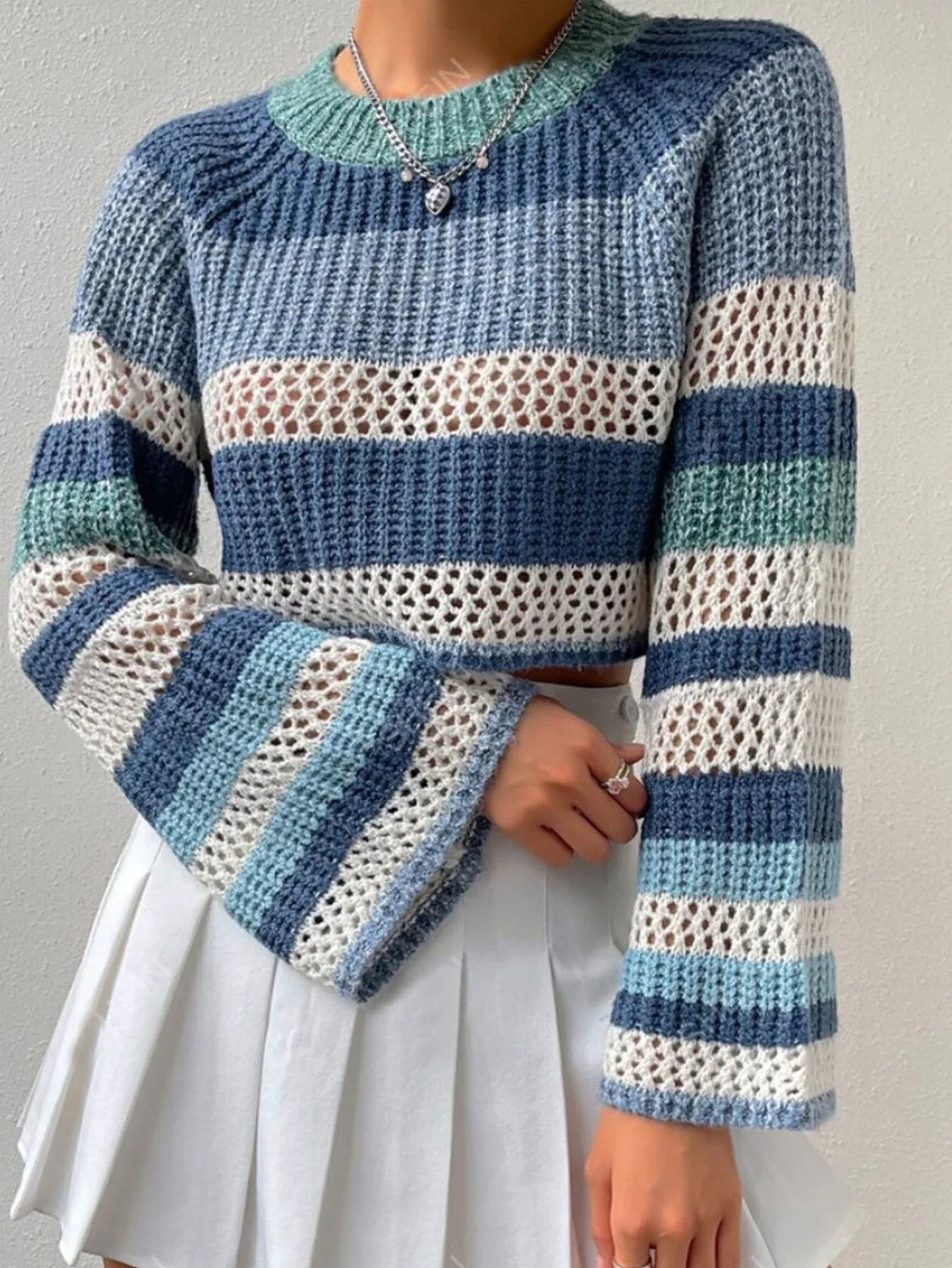 Close-up of a woman wearing a blue and white striped crochet knit cropped sweater with bell sleeves and a silver necklace.