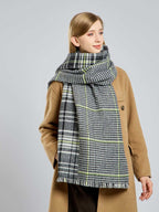 Woman in a tan coat with her large houndstooth and plaid scarf wrapped around her neck