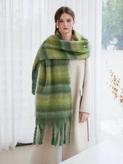 Woman modeling a cream coat and a green striped scarf with fringe detail.