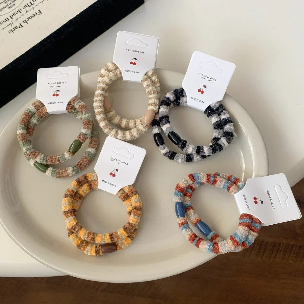 A group of fuzzy striped hair ties with beaded accents, presented on a white plate and a tray.