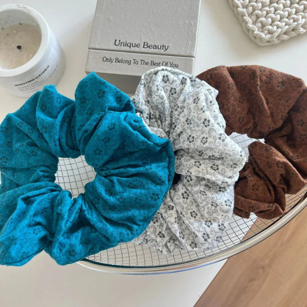 three scrunchies in teal, white with floral pattern, and brown
