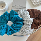 three scrunchies in teal, white with floral pattern, and brown