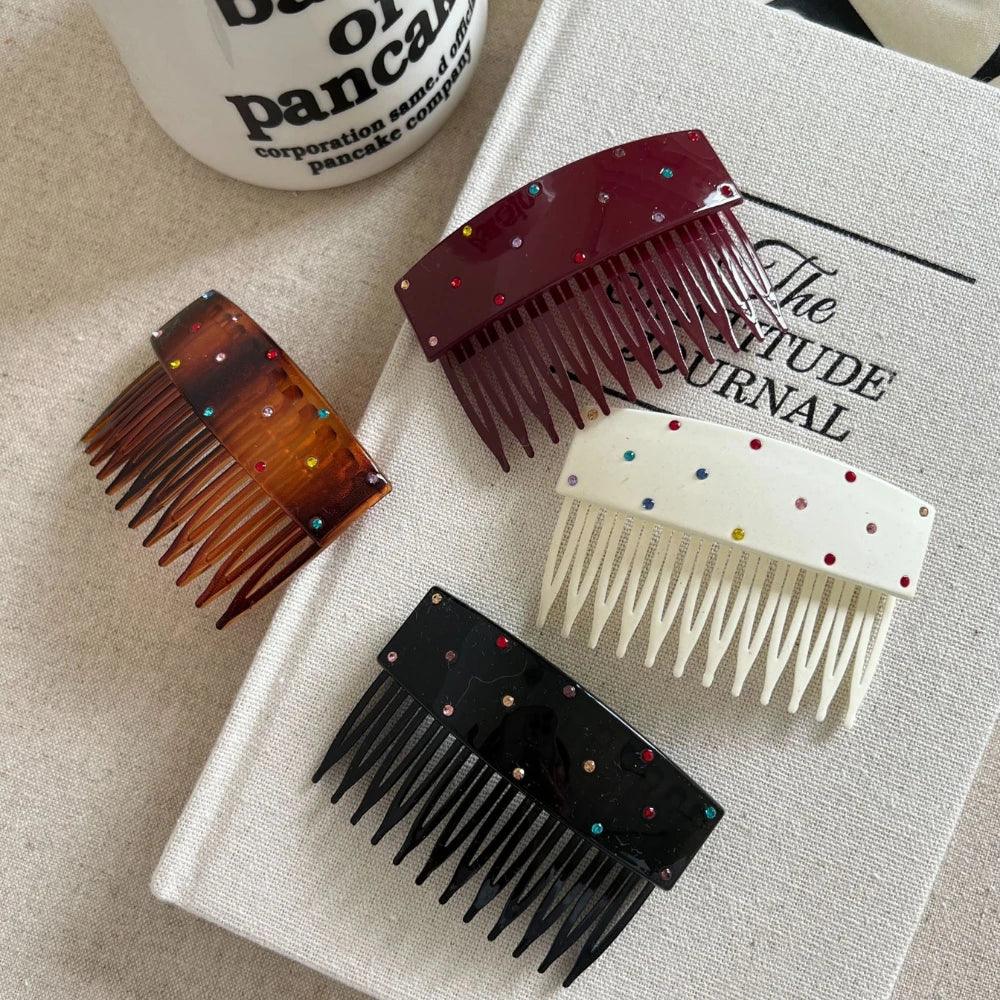 Four colorful and sparkly hair combs laid out on a textured surface alongside other lifestyle items.
