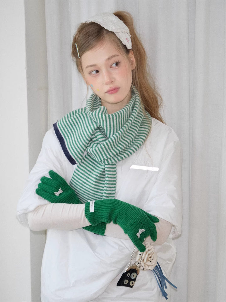 Model wearing a green and white striped knit scarf, white t-shirt, and green knit gloves with bow details.