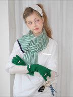 Model wearing a green and white striped knit scarf, white t-shirt, and green knit gloves with bow details.