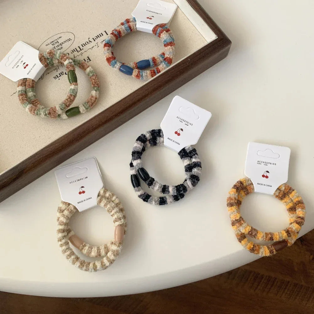 Several fuzzy hair ties with different striped patterns and bead colors, arranged on a white table.
