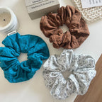 three scrunchies in teal, white with floral pattern, and brown on a white surface