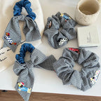 Arrangement of black and white gingham scrunchies with denim and embroidered dog details, styled on a table