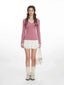 Woman wearing a pink long-sleeved top with white lace trim and white pleated shorts, holding a cream handbag and wearing cream leg warmers and silver shoes.