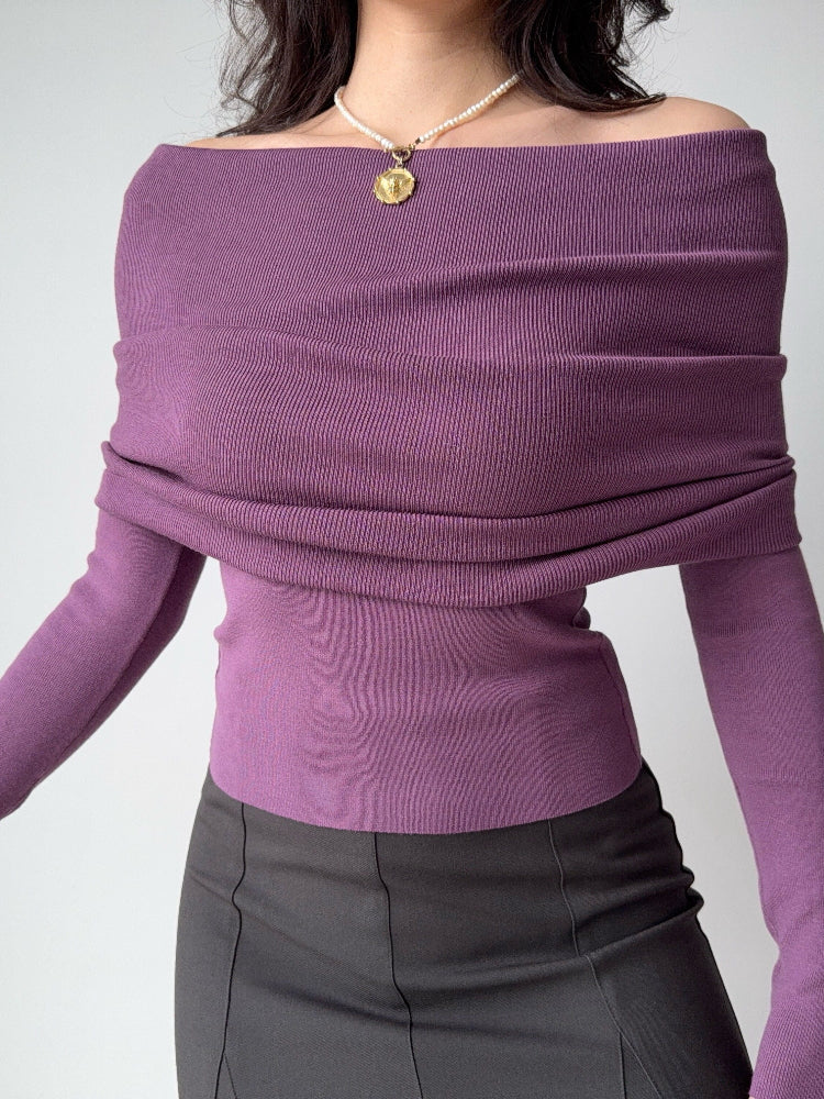 Close-up of a woman's torso wearing a purple off-the-shoulder knit top with a draped neckline and long sleeves.