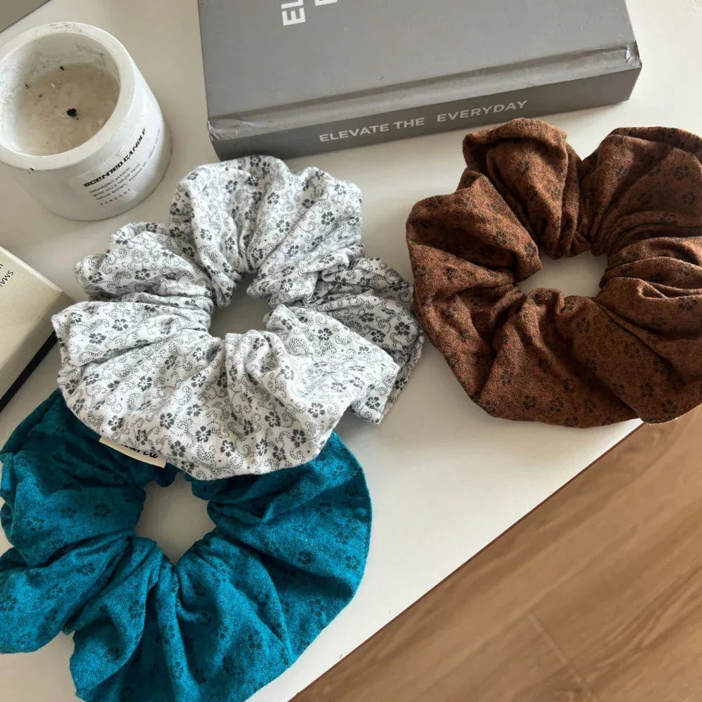 three scrunchies in teal, white with floral pattern, and brown on a white surface with decor