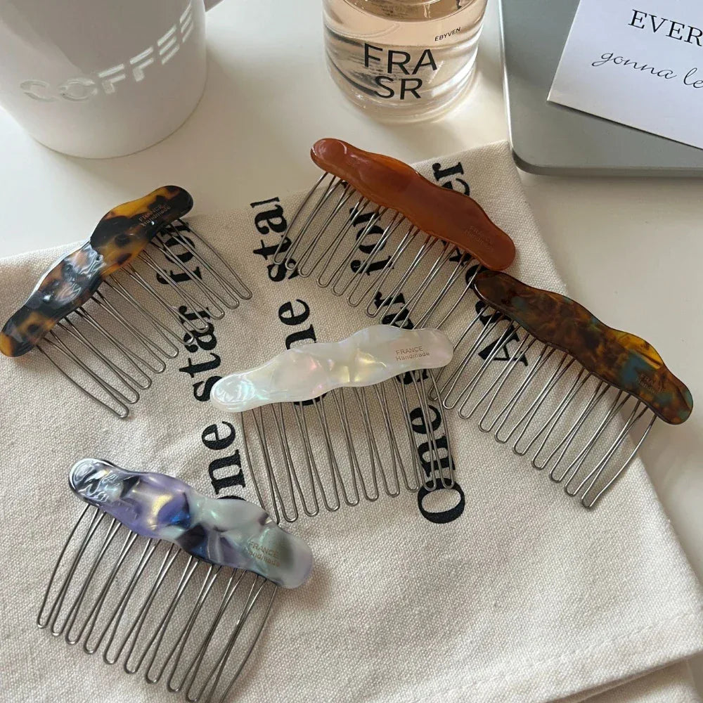 A spread of cloud-shaped hair combs in various colors, arranged on a textured cloth with a coffee mug and a perfume bottle in the background.