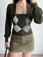 Woman wearing a green argyle knit tube top, cropped bolero cardigan, and khaki skirt, holding a black handbag.