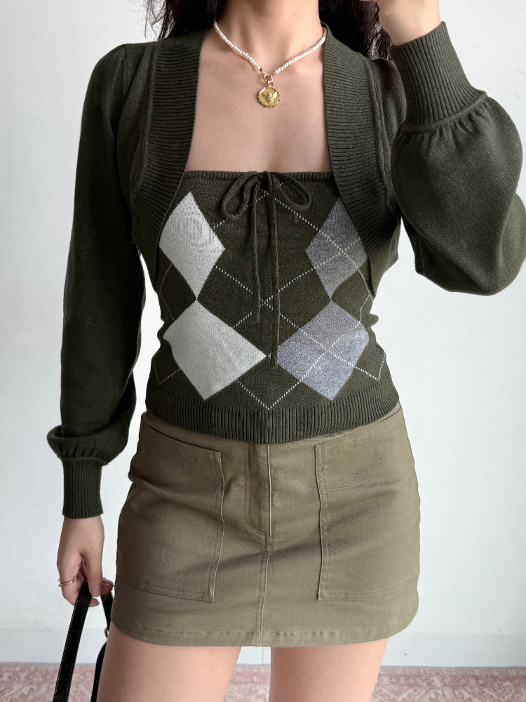 Woman wearing a green argyle knit tube top, cropped bolero cardigan, and khaki skirt, holding a black handbag.