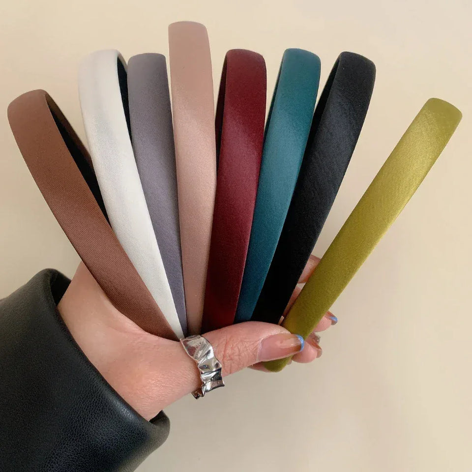 Hand holding multiple satin padded headbands in various colors including brown, white, grey, pink, burgundy, teal, black, and olive green Secondary image