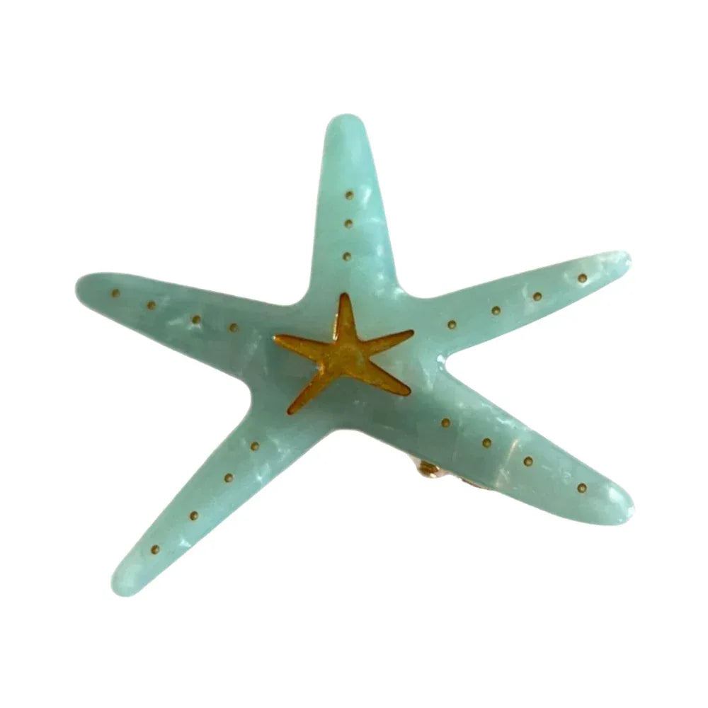 A light blue translucent acrylic starfish hair clip with a gold central star and gold dots.