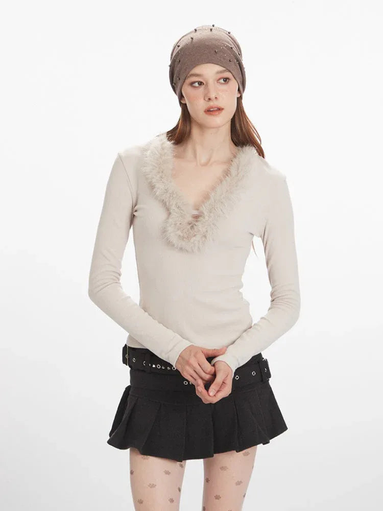 Close-up of a woman wearing a cream long-sleeve top with fur trim, a black pleated mini skirt, decorative tights, and black boots, holding a white bucket bag.