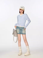 Full body shot of a model wearing a light blue cropped cardigan, white top, denim mini skirt, beige baseball cap, and white socks with sneakers.
