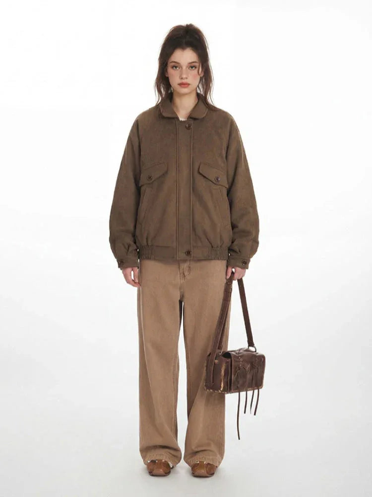 Woman wearing a brown bomber jacket and tan pants, holding a brown bag. Main image